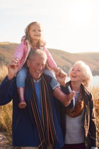 Grandfather giving granddaughter a ride on his shoulders while walking on a trail with her grandmother.